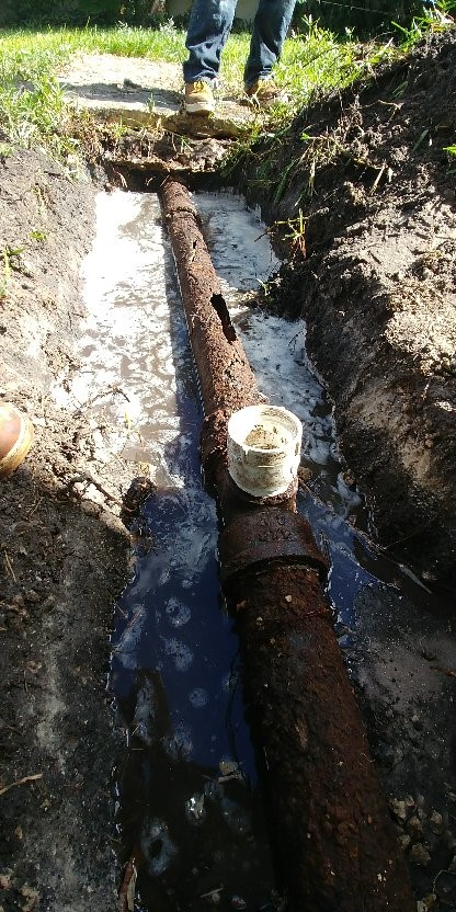 Image of cast iron pipe in ground surrounded by water and then dirt/grass with PVC fitting sticking up.