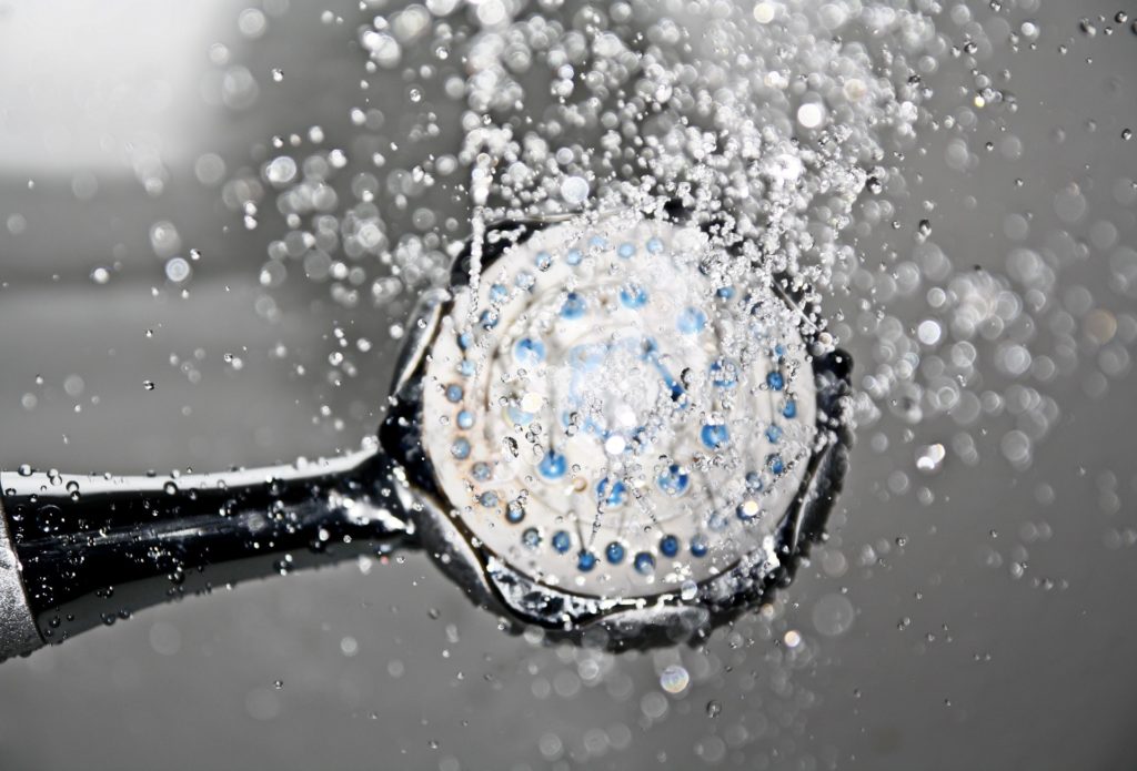 Image shows a shower head with mineral deposits on it spraying water.